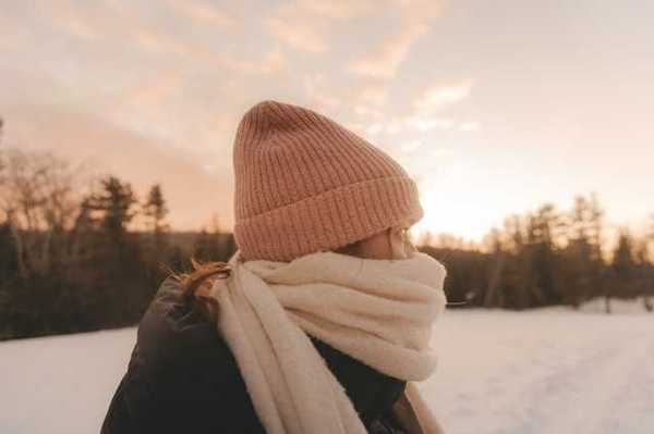 A woman in a snowy lanscape wearing a hat and scarf bundled against the cold weather