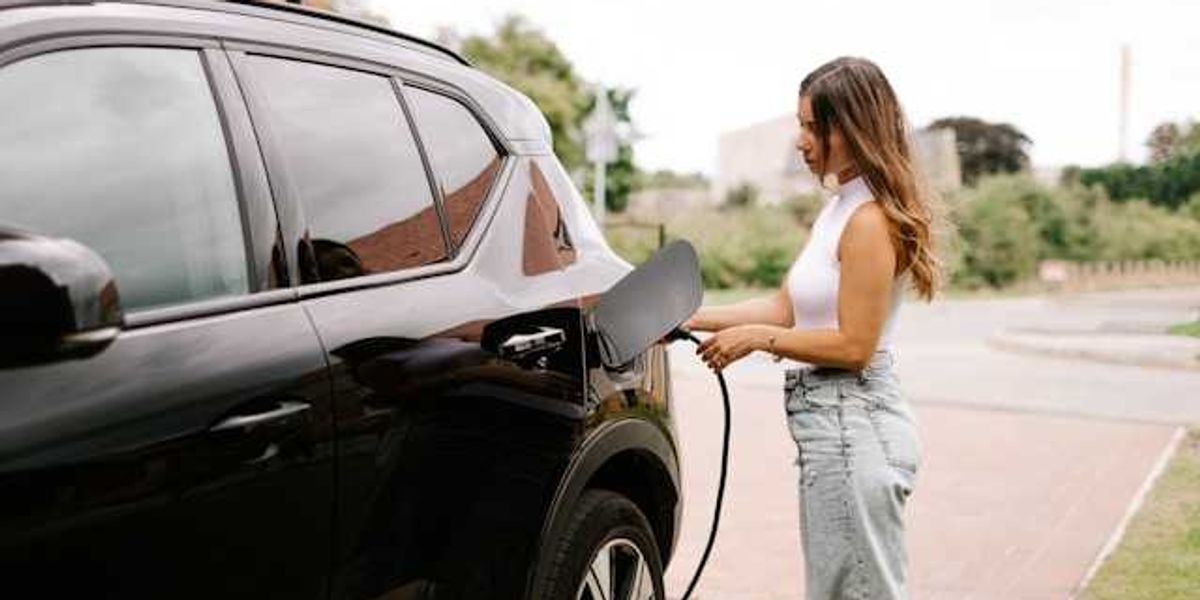 A woman inserting a charging cable into an electric vehicle