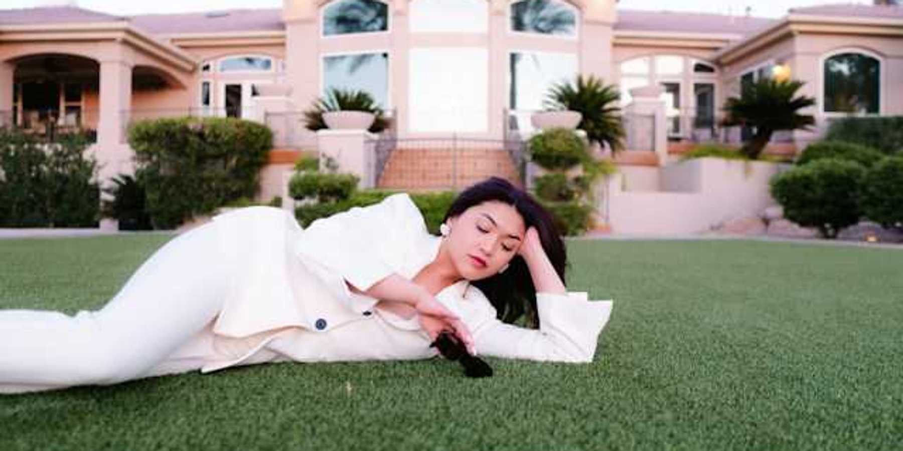 A woman laying on the grass in front of a large house