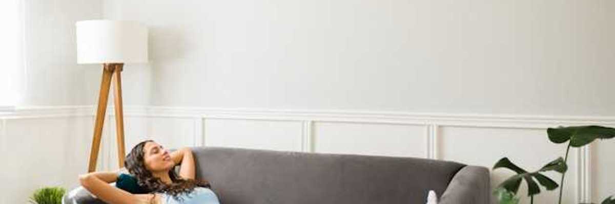 A woman lying on a couch under a wall mounted air conditioning unit