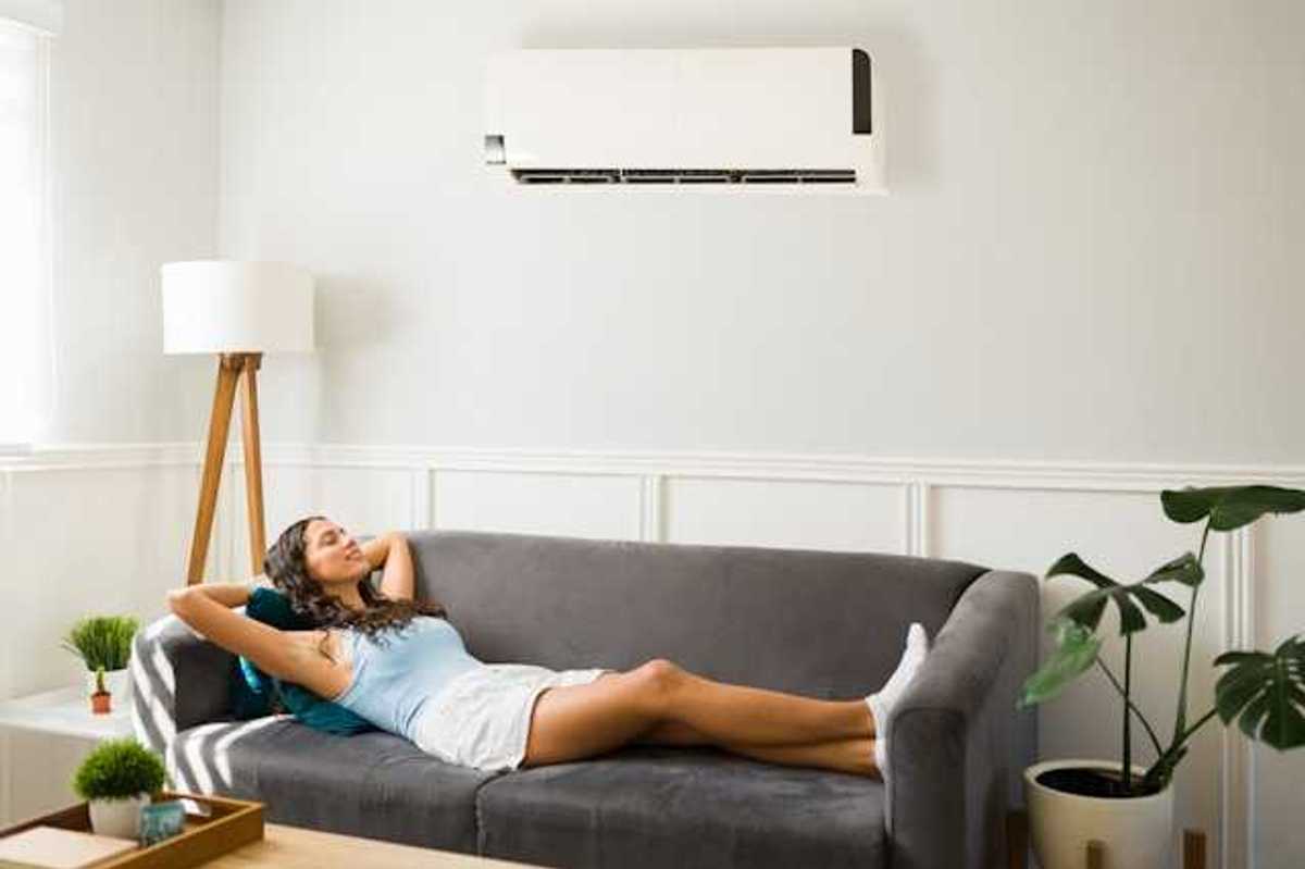 A woman lying on a couch under a wall mounted air conditioning unit