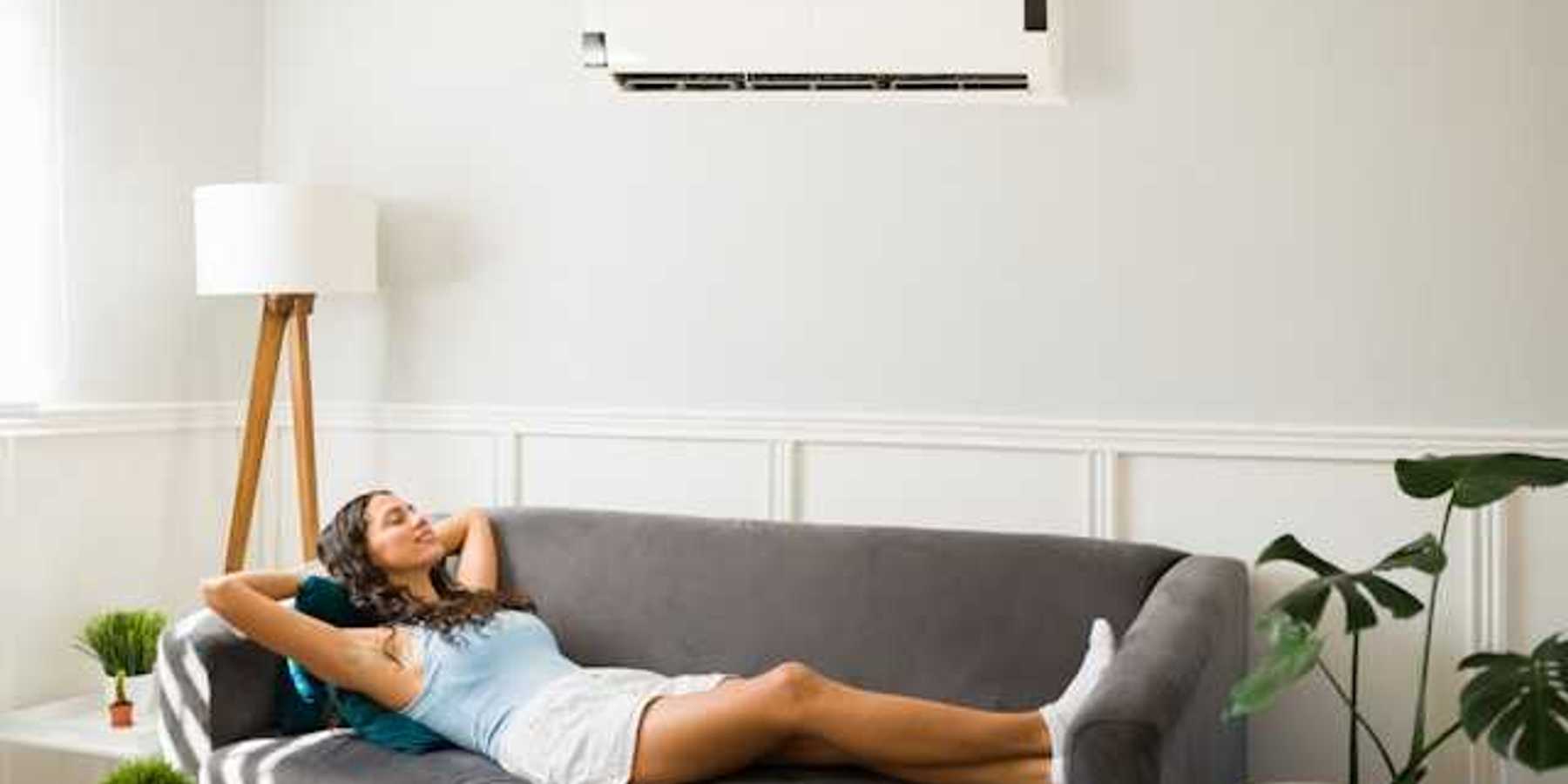 A woman lying on a couch under a wall mounted air conditioning unit