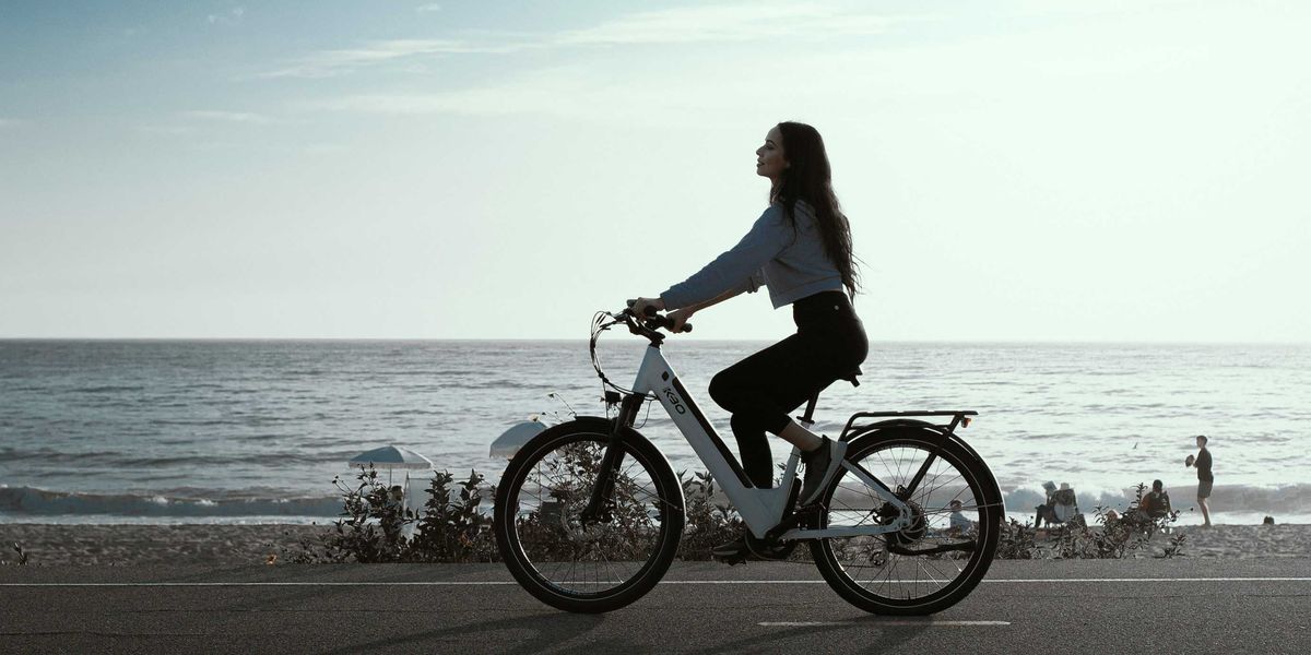 a woman riding an e-bike down a street next to the ocean