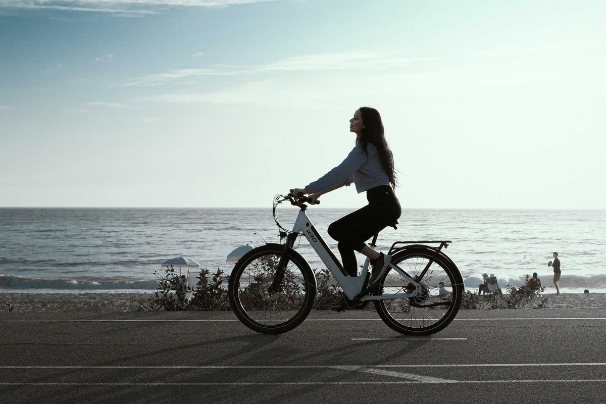 a woman riding an e-bike down a street next to the ocean