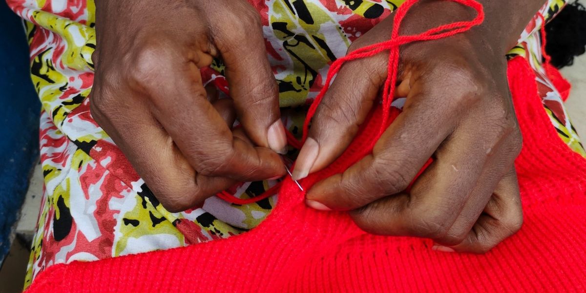 A woman's hands mend a red sweater.