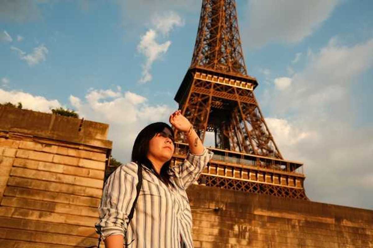 A woman shielding her eyes from the sun with the Eiffel Tower in the background