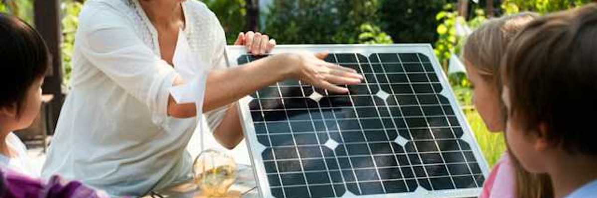 A woman showing a small solar panel to a group of children