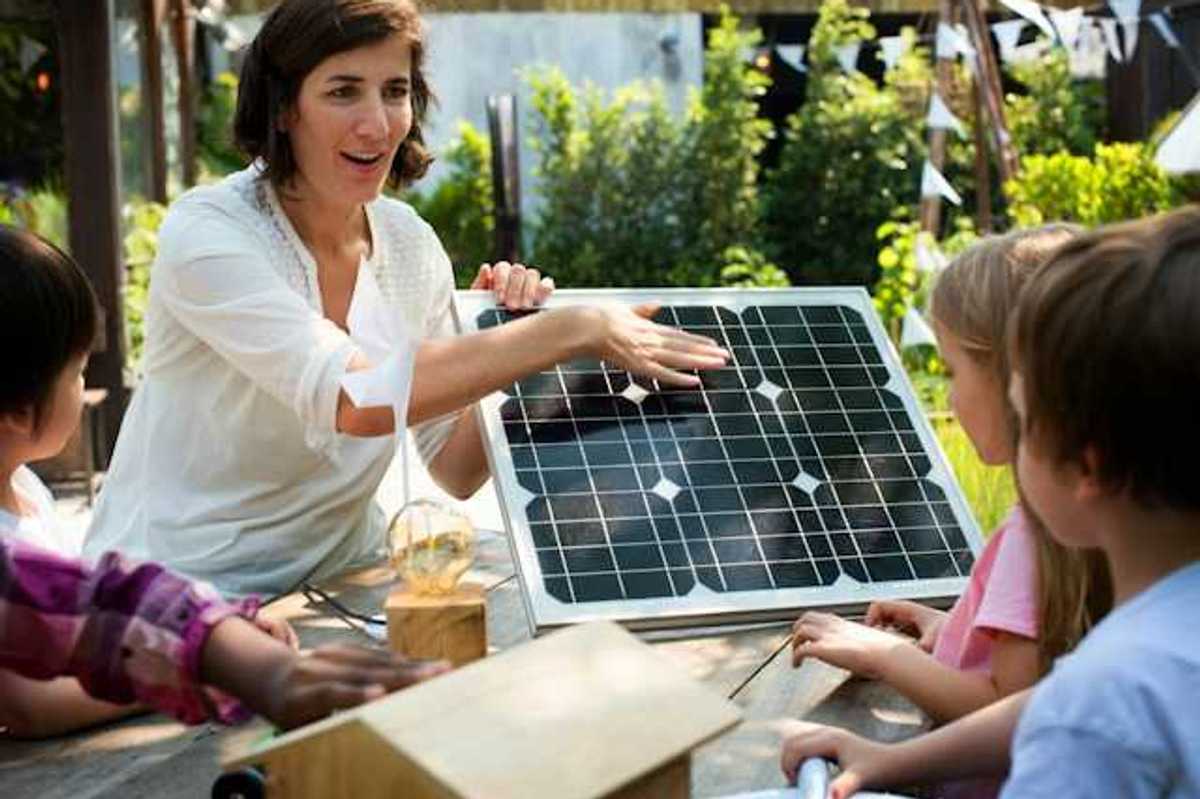 A woman showing a small solar panel to a group of children