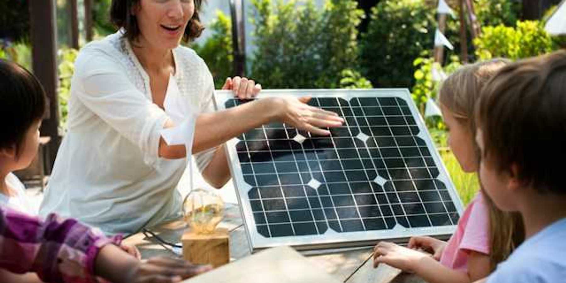 A woman showing a small solar panel to a group of children