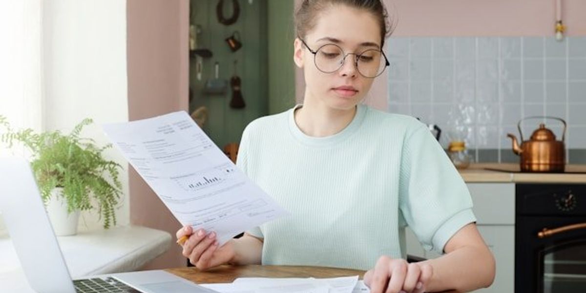 A woman sitting at a kitchen table with a utility bill and a calculator.