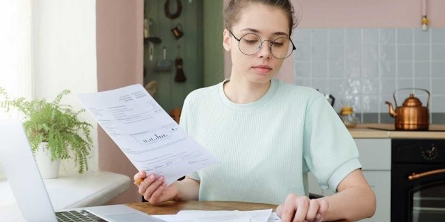 A woman sitting at a kitchen table with a utility bill and a calculator.