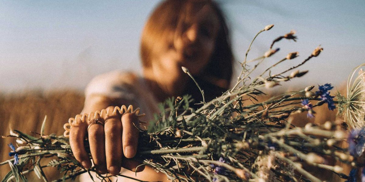 a woman sitting in a field holding a bunch of flowers.