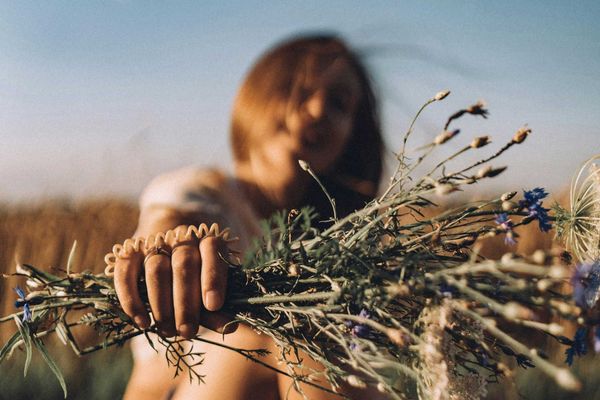 a woman sitting in a field holding a bunch of flowers.