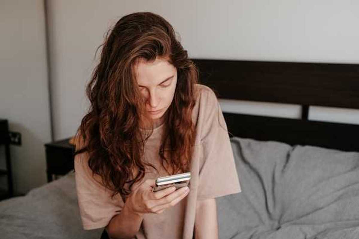 A woman sitting in bed looking at her phone