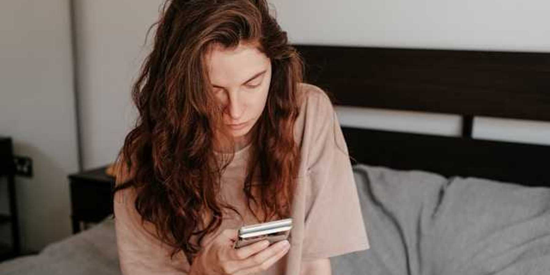 A woman sitting in bed looking at her phone