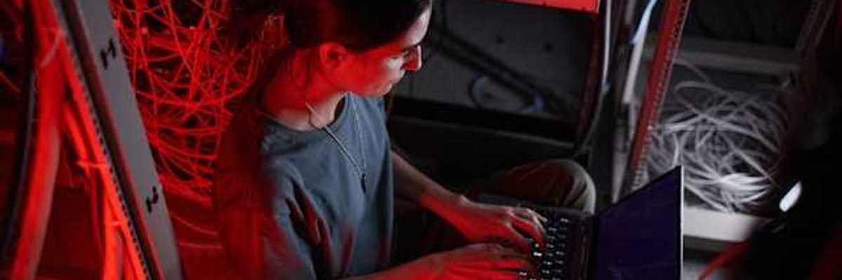 A woman sitting in front of a laptop with servers behind her