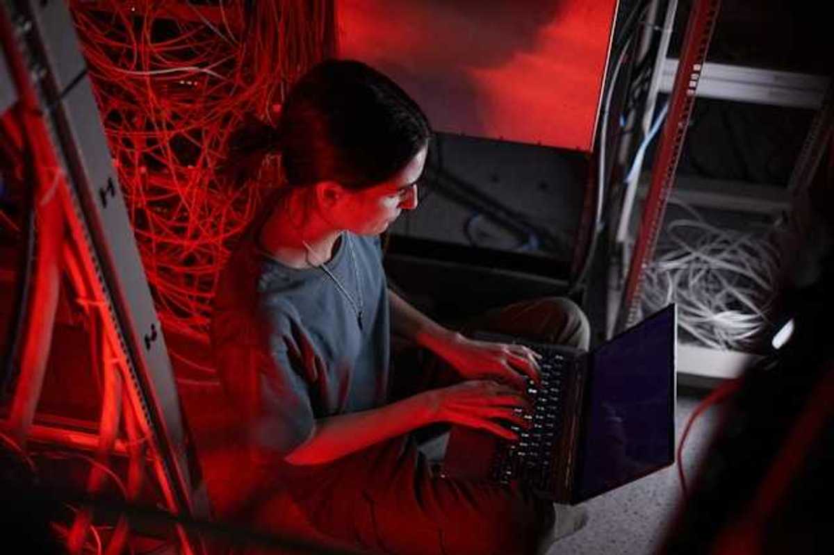 A woman sitting in front of a laptop with servers behind her