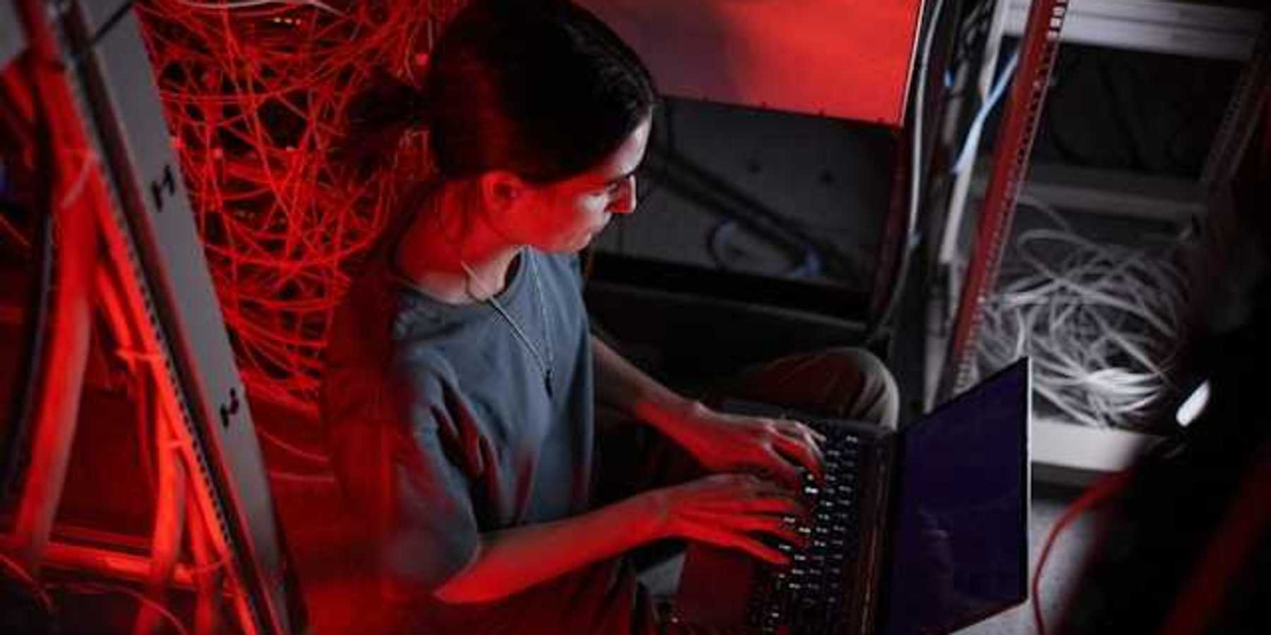 A woman sitting in front of a laptop with servers behind her