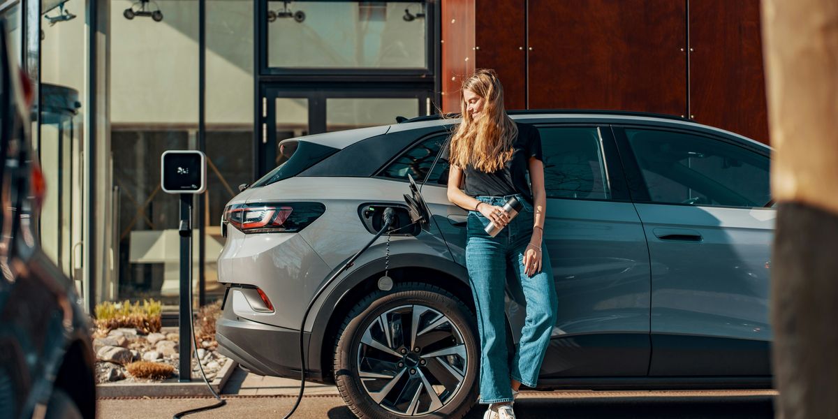 a woman standing next to a blue electric vehicle being charged.