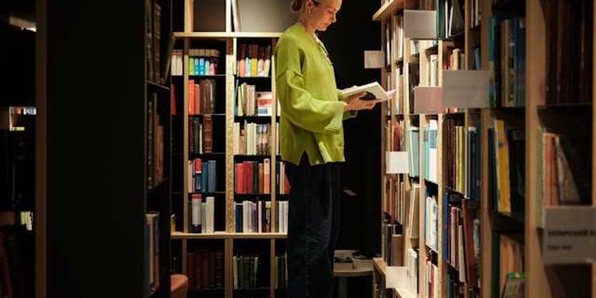 A woman standing on a stool in front of library bookshelves