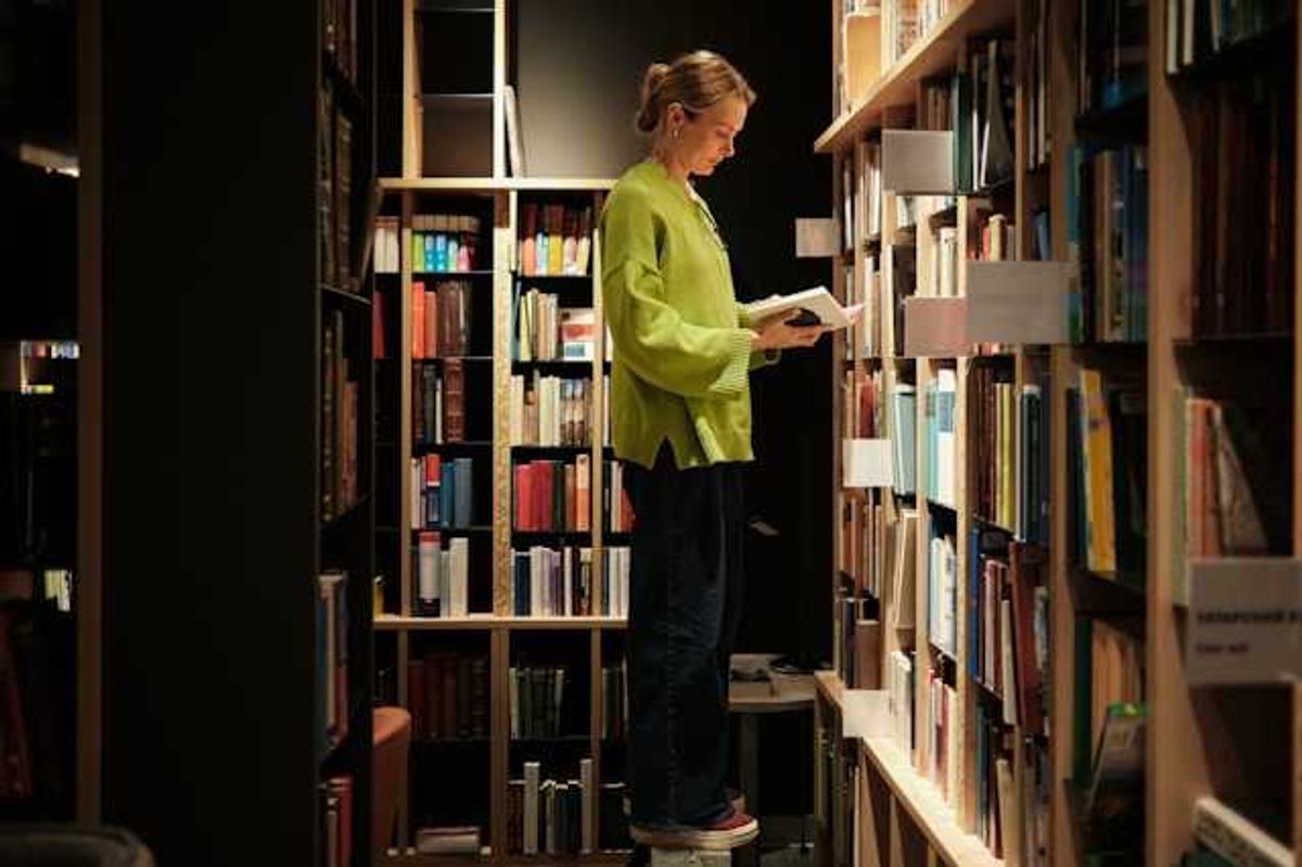 A woman standing on a stool in front of library bookshelves