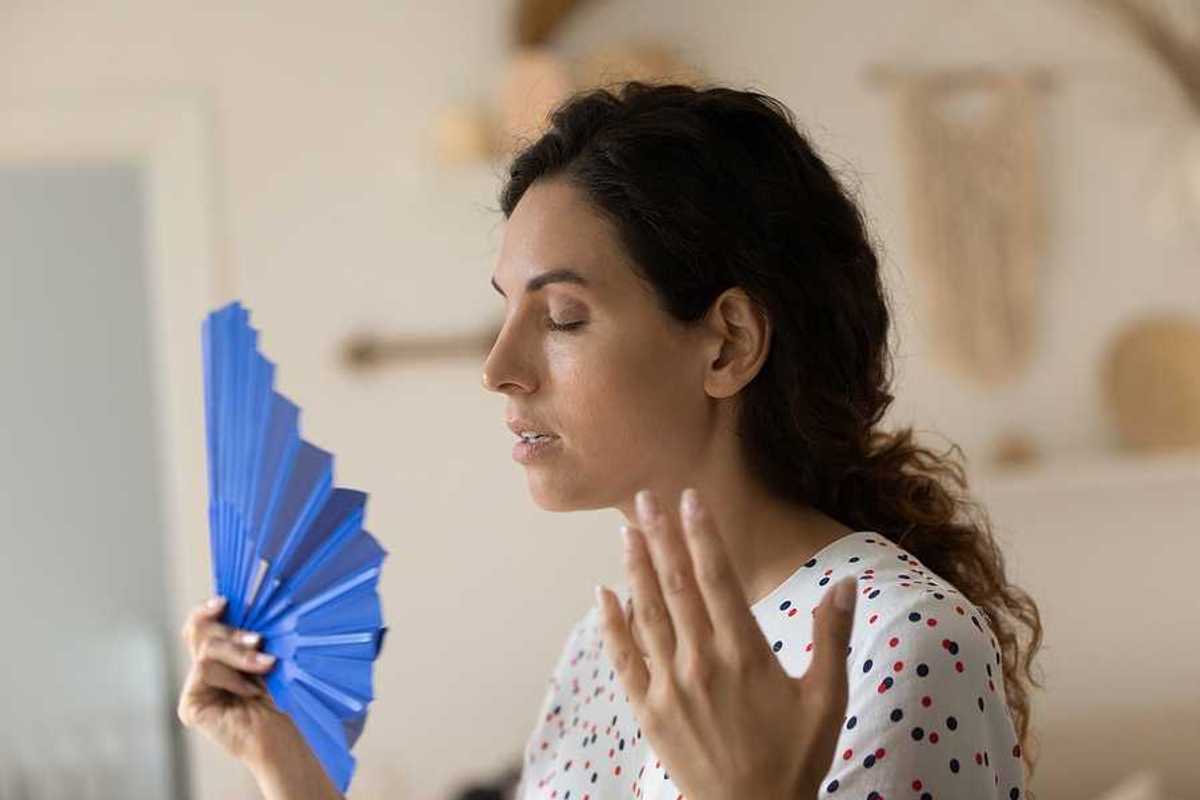 A woman using a blue fan to try to cool herself off