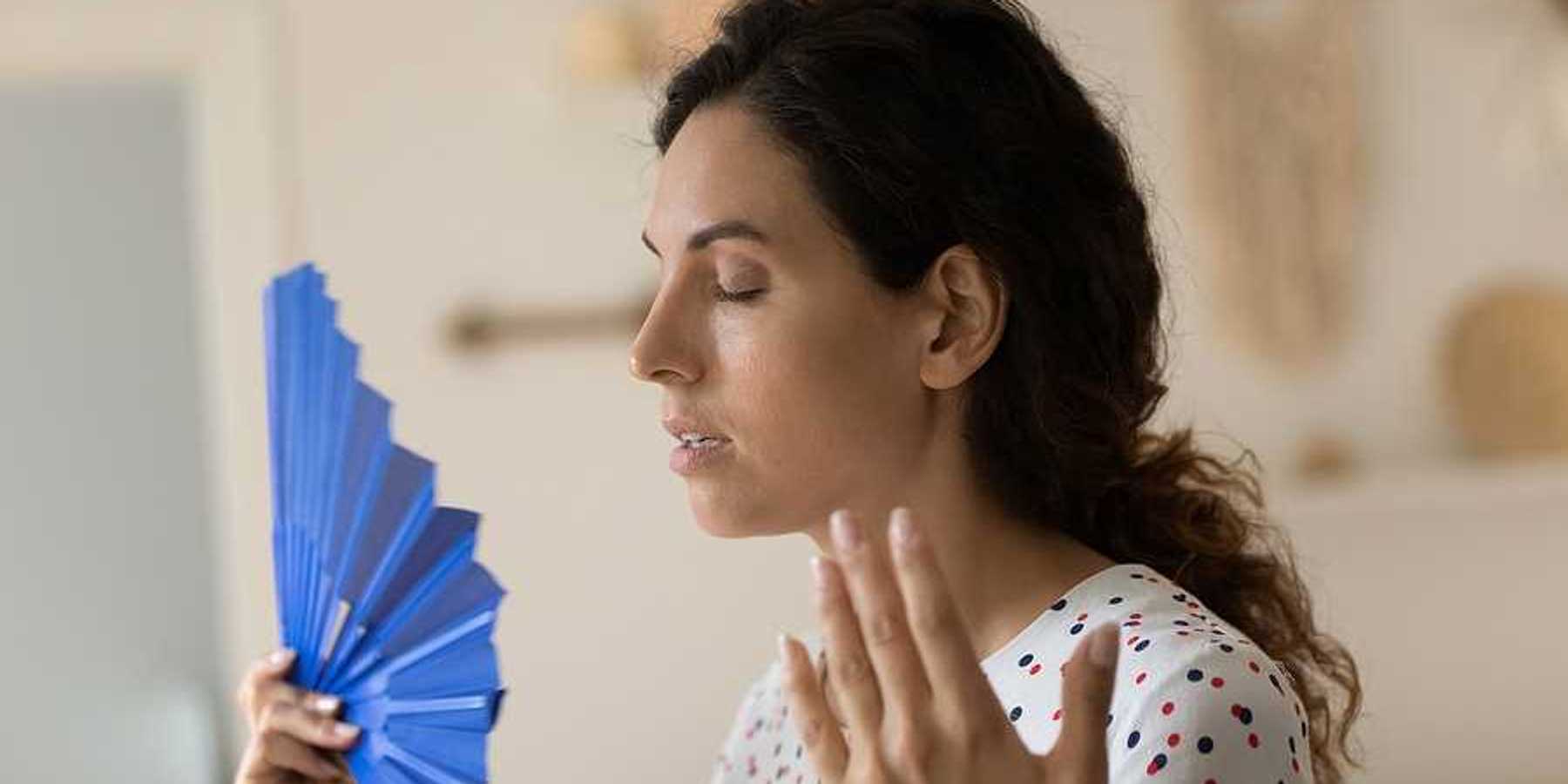 A woman using a blue fan to try to cool herself off