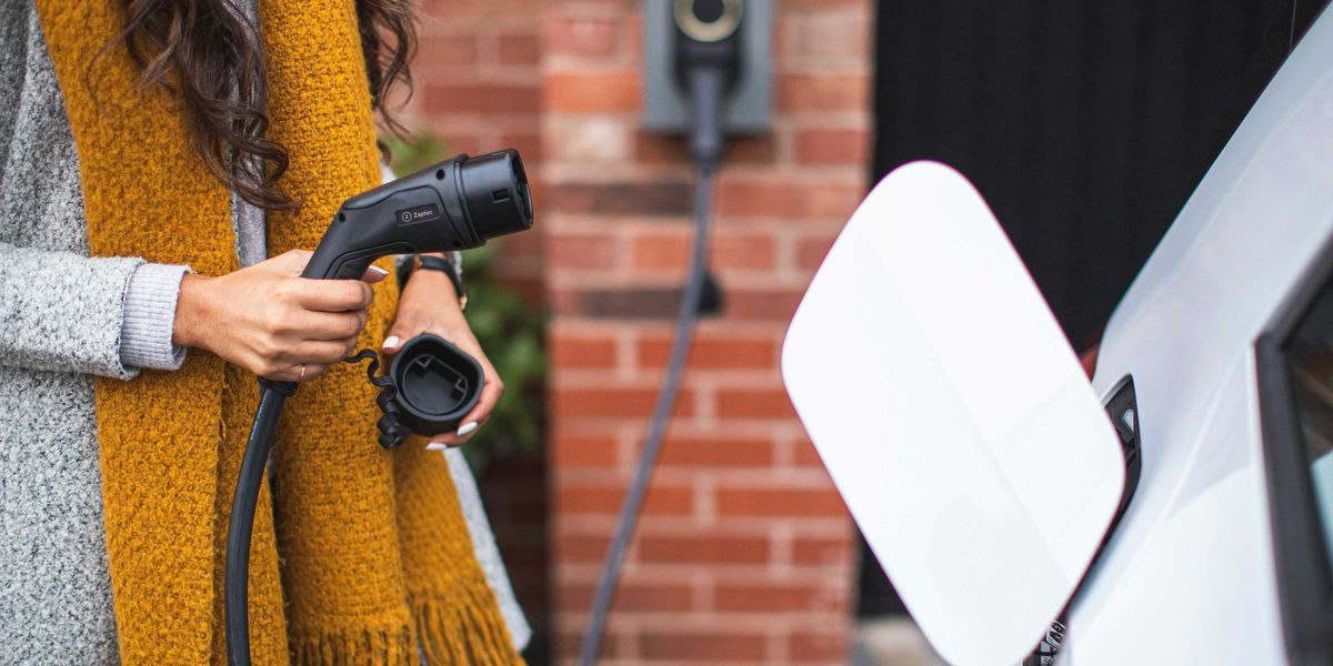 a woman with a yellow scarf attaching an electric vehicle charger to her car