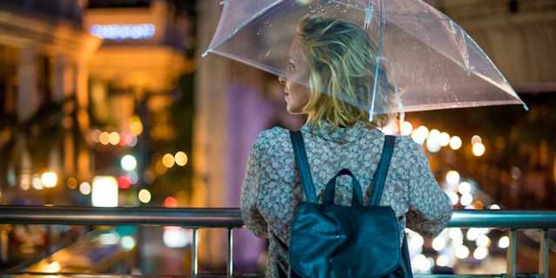 A woman with an umbrella looking out over a city street at night