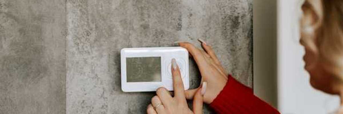 A woman with her finger on a wall thermostat, changing the temperature