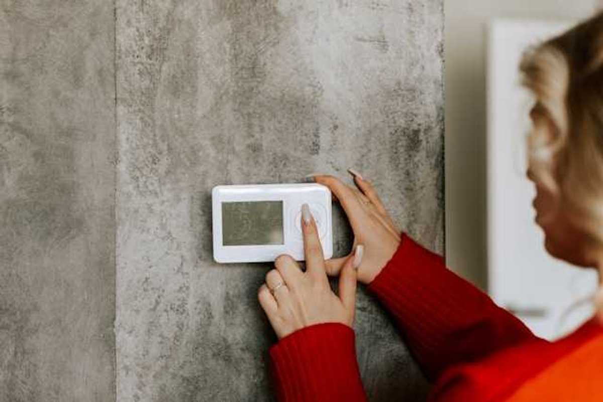 A woman with her finger on a wall thermostat, changing the temperature