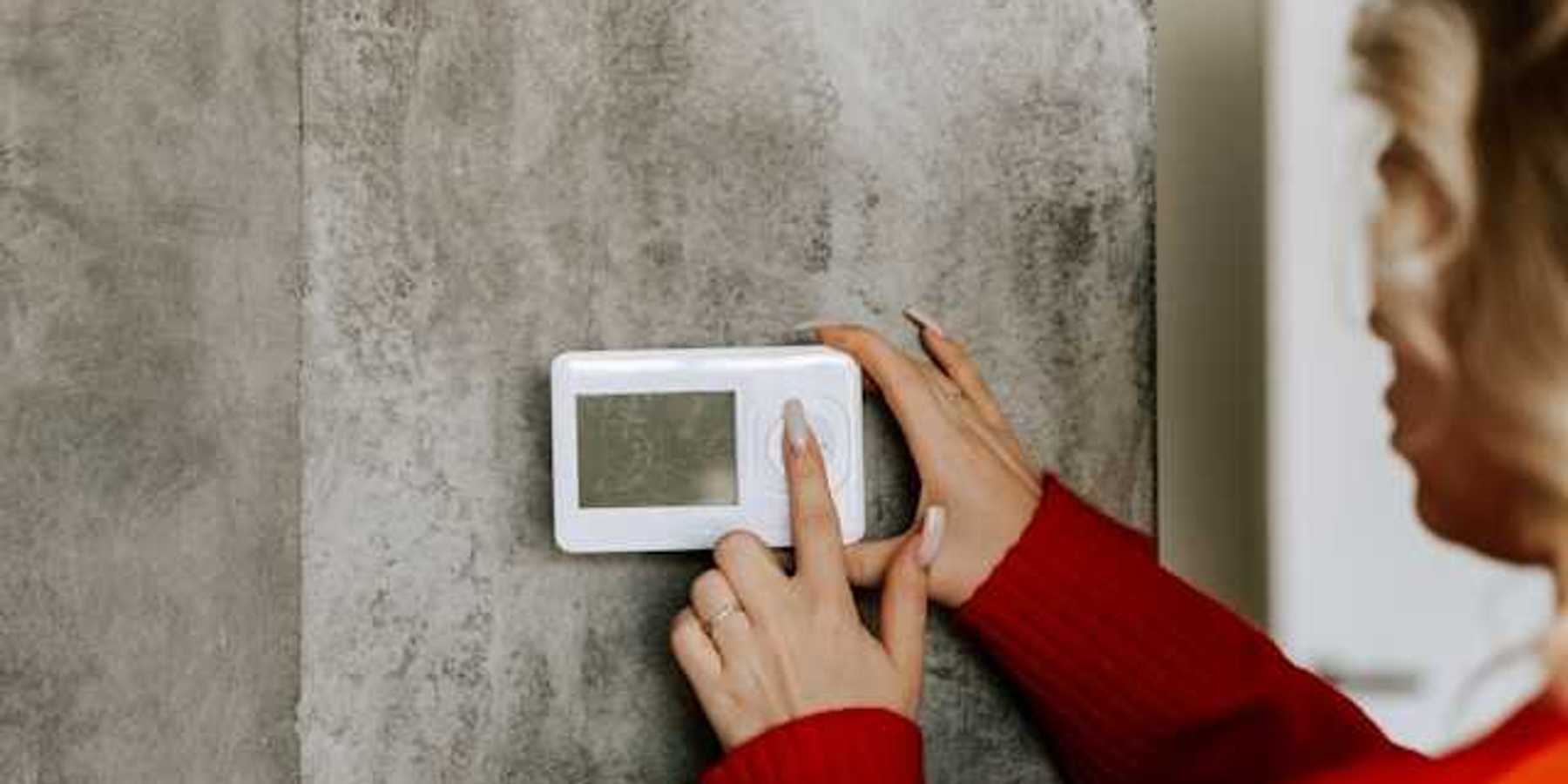 A woman with her finger on a wall thermostat, changing the temperature