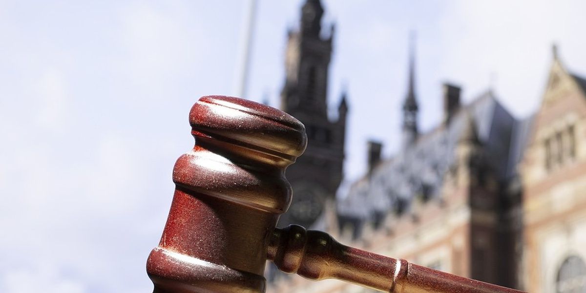 A wooden gavel on a surface with the Hague International Court of Justice in background.