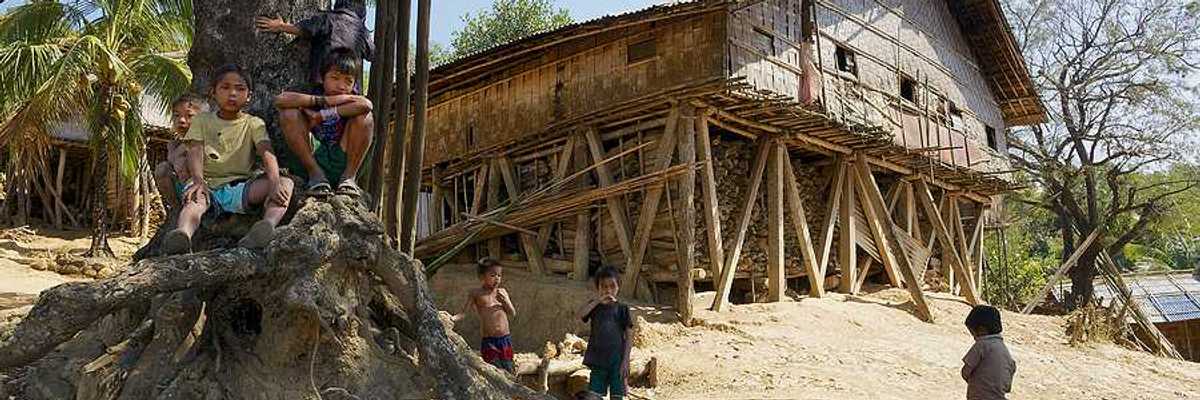 A wooden hut located on a hill with small children playing in the dirt in front of it