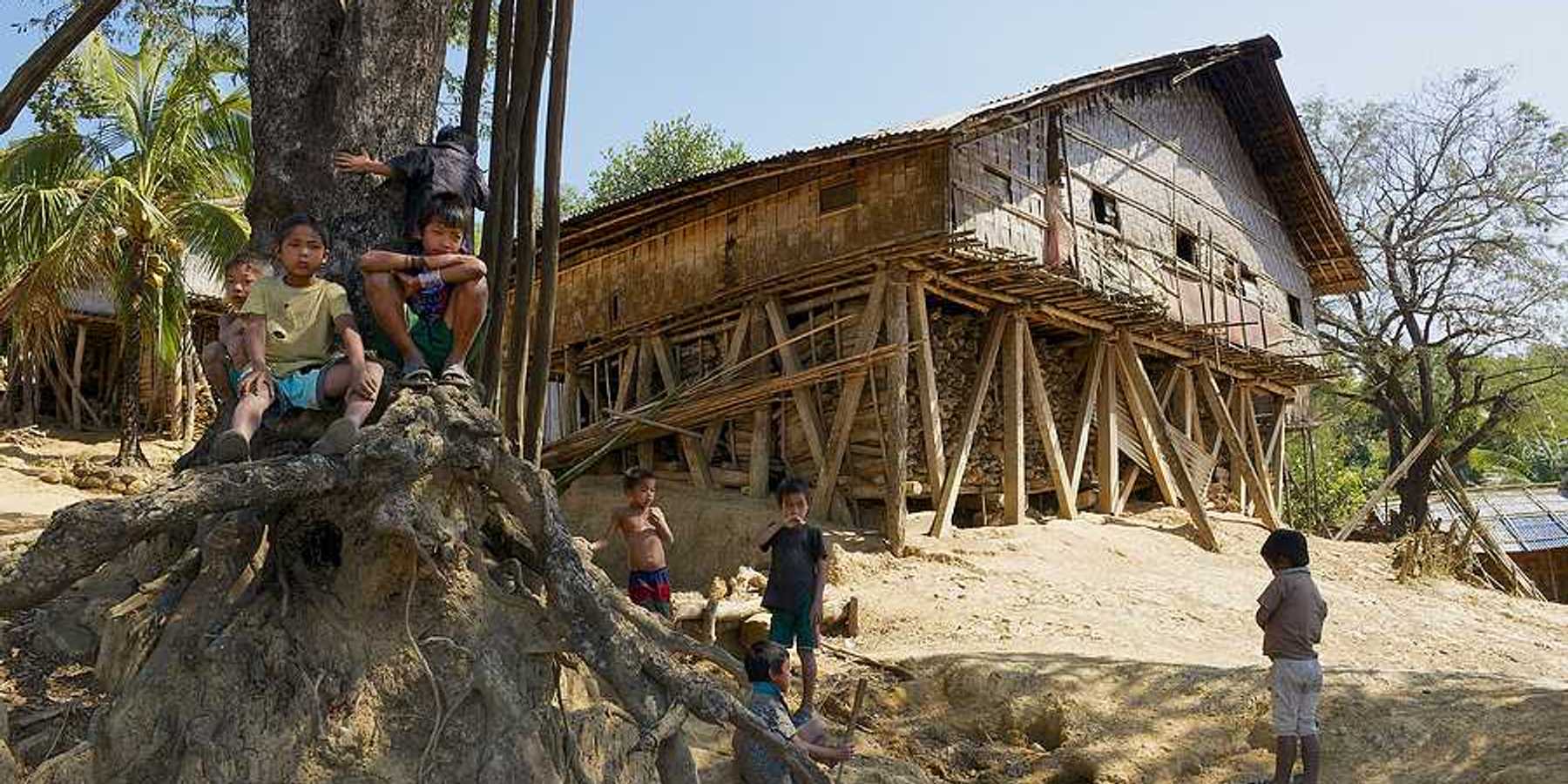 A wooden hut located on a hill with small children playing in the dirt in front of it