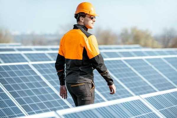 A worker in an orange hard hat inspecting solar polars