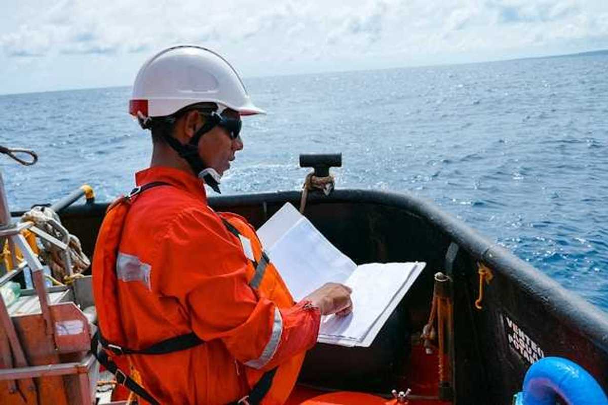A worker in an orange jumpsuit and hardhat on an oil drill