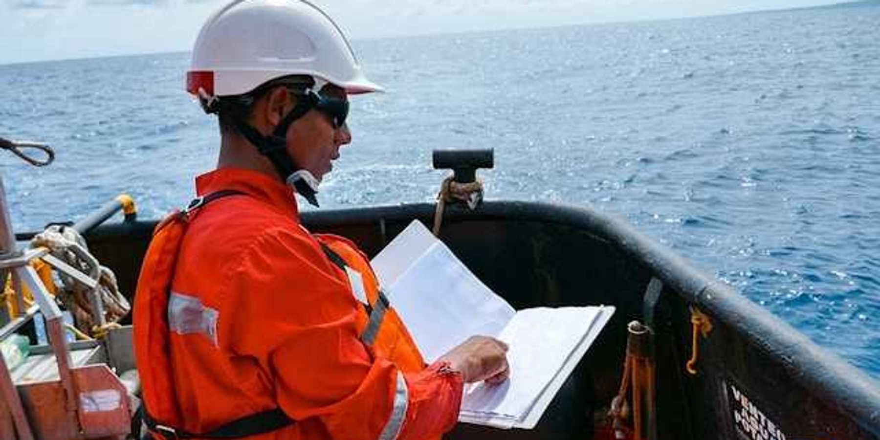 A worker in an orange jumpsuit and hardhat on an oil drill