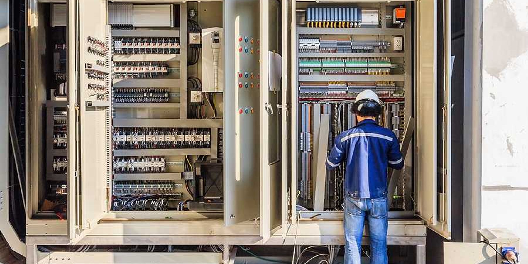 A worker installing electronics in a large industrial cabinet