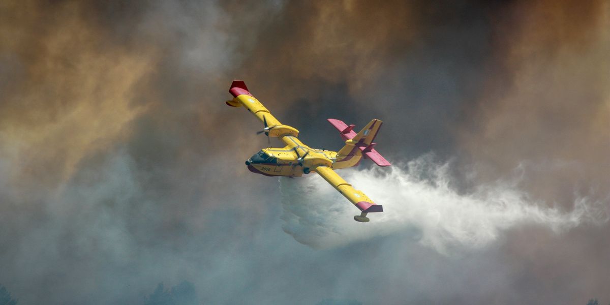 A yellow airplane dropping water on a wildfire surrounded by smoke.