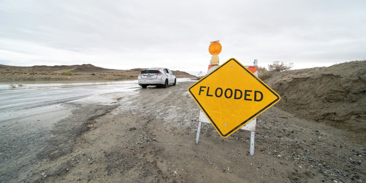 a yellow flood sign sitting on the side of a wet road with uneven pavement.