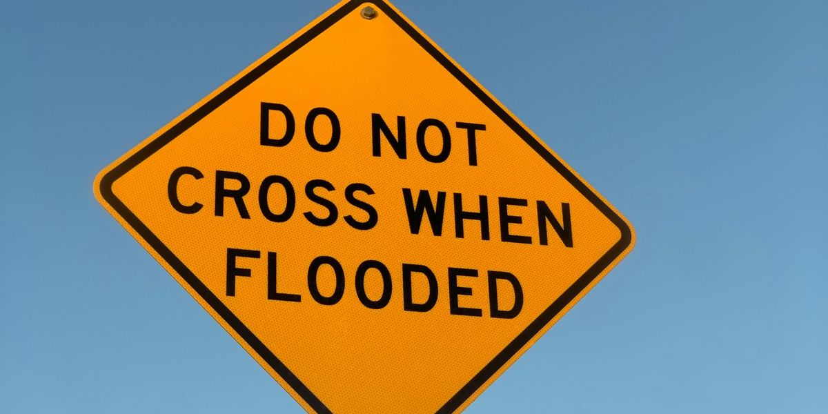 a yellow sign with black text saying 'Do not cross when flooded'.