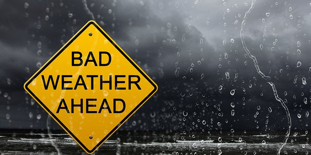 A yellow sign with the words 'Bad Weather Ahead' on the beach with a storm in the background.