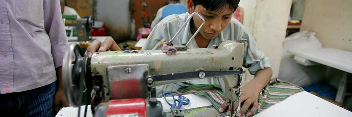 A young Asian boy sitting at a sewing machine in a factory