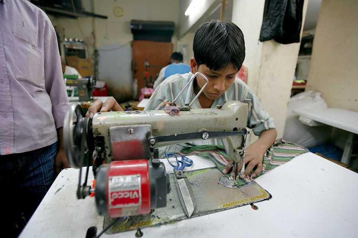 A young Asian boy sitting at a sewing machine in a factory