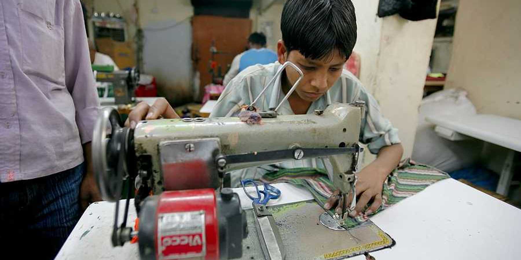 A young Asian boy sitting at a sewing machine in a factory