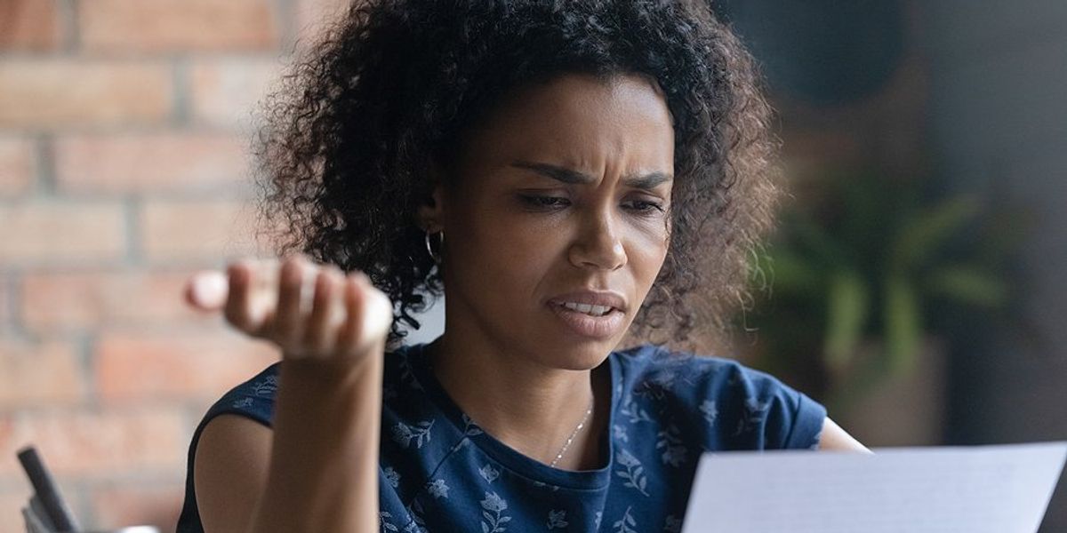 A young black woman making a gesture of frustration with her hand while looking at a piece of paper.