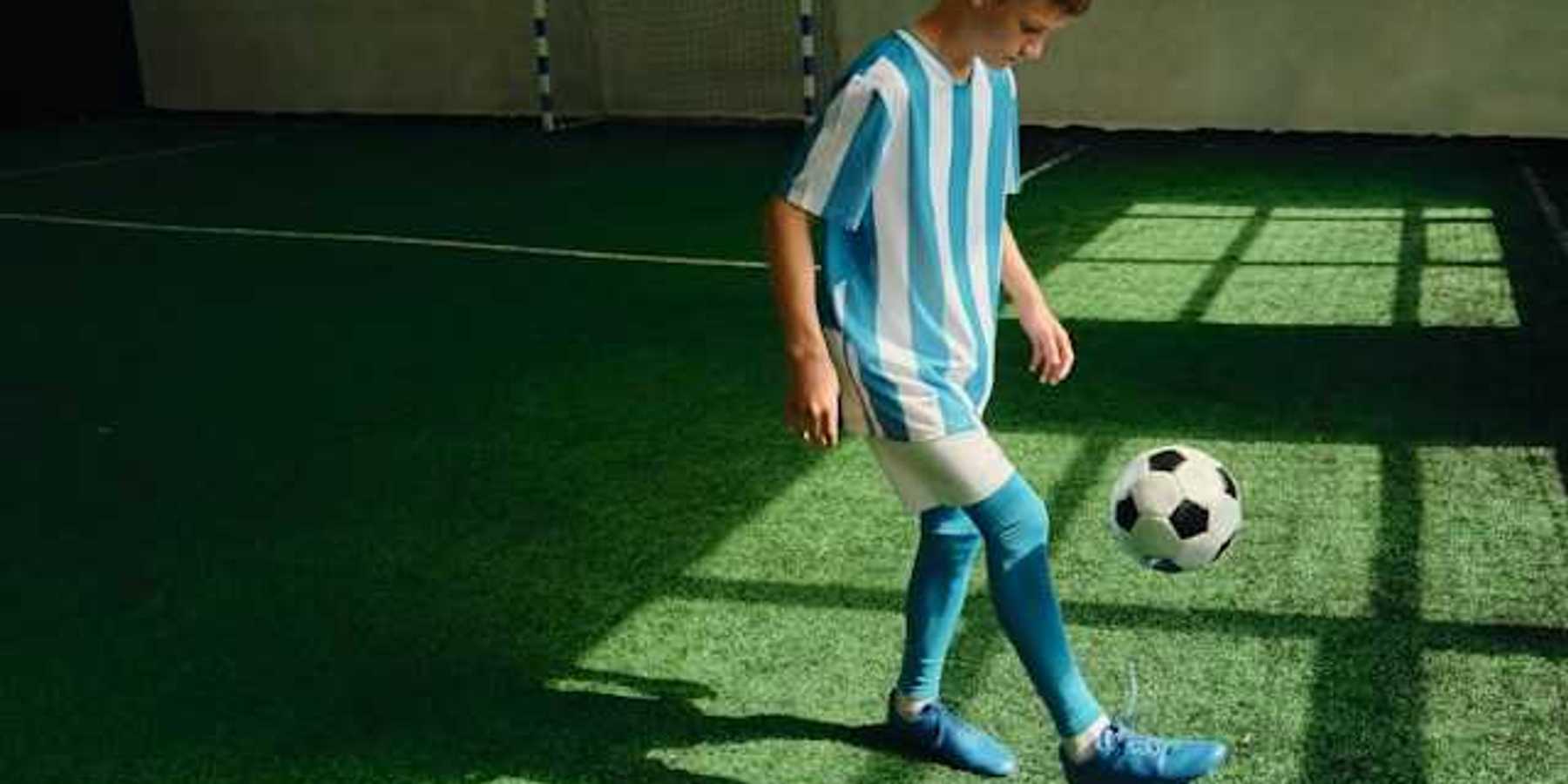 A young boy kicking a soccer ball on an artificial turf surface