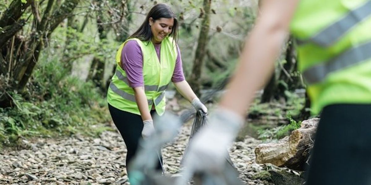 A young woman in a yellow vest helping gather trash in the forest.