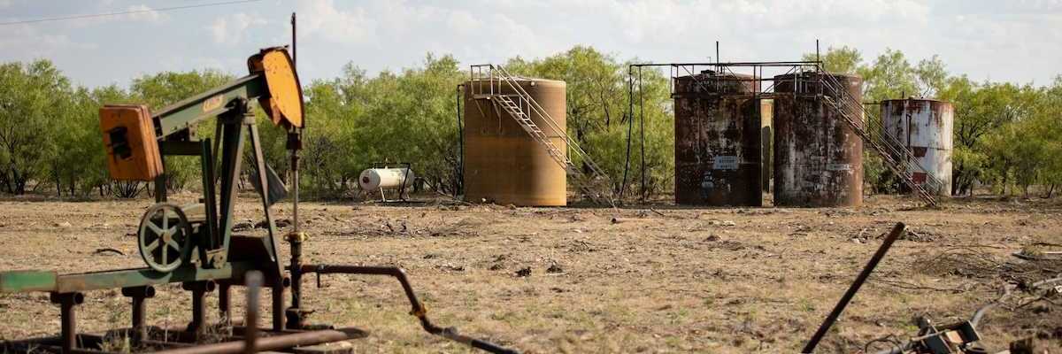 Abandoned oil well adjacent to rusting storage tanks
